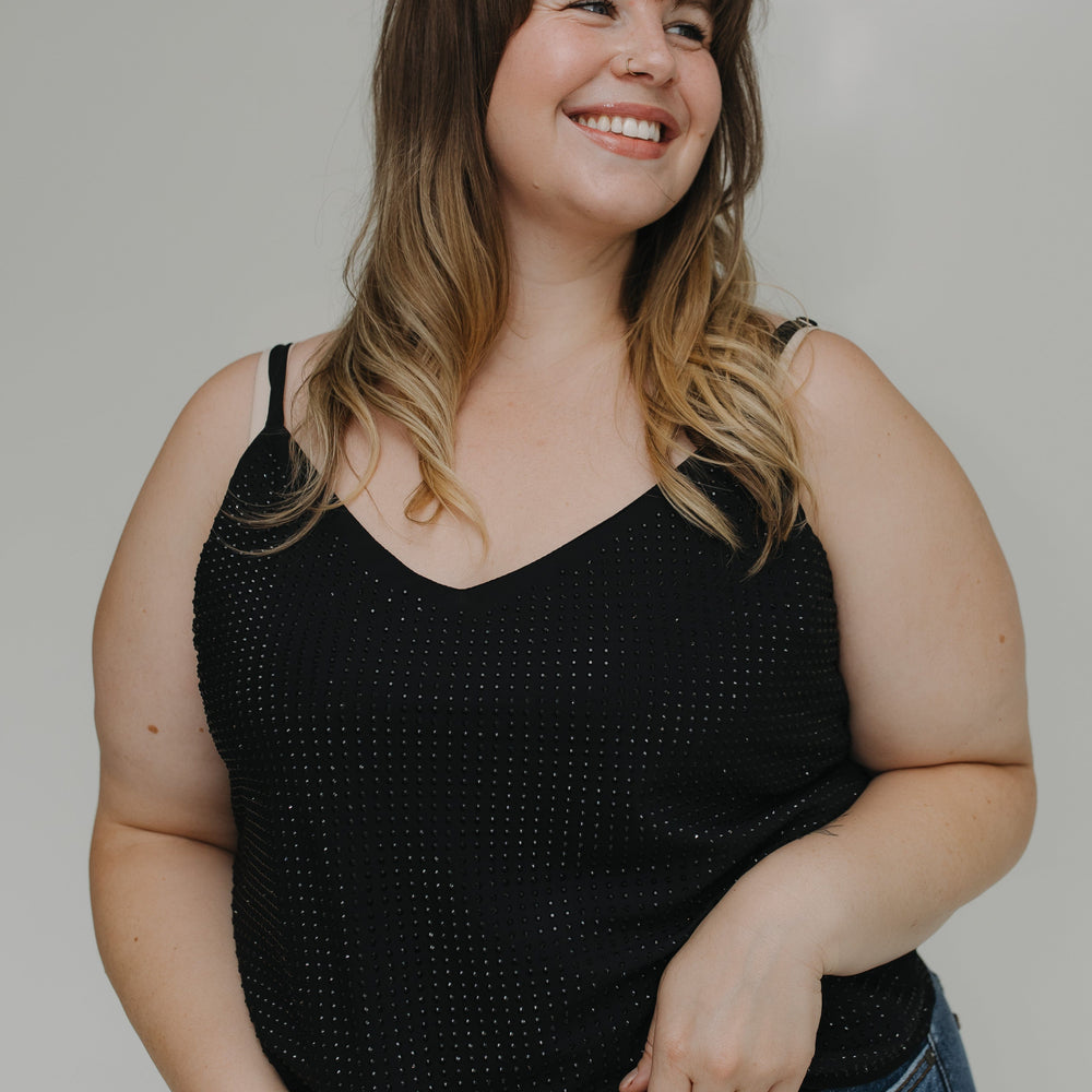 Woman wearing a black tank top and blue jeans with a neutral background