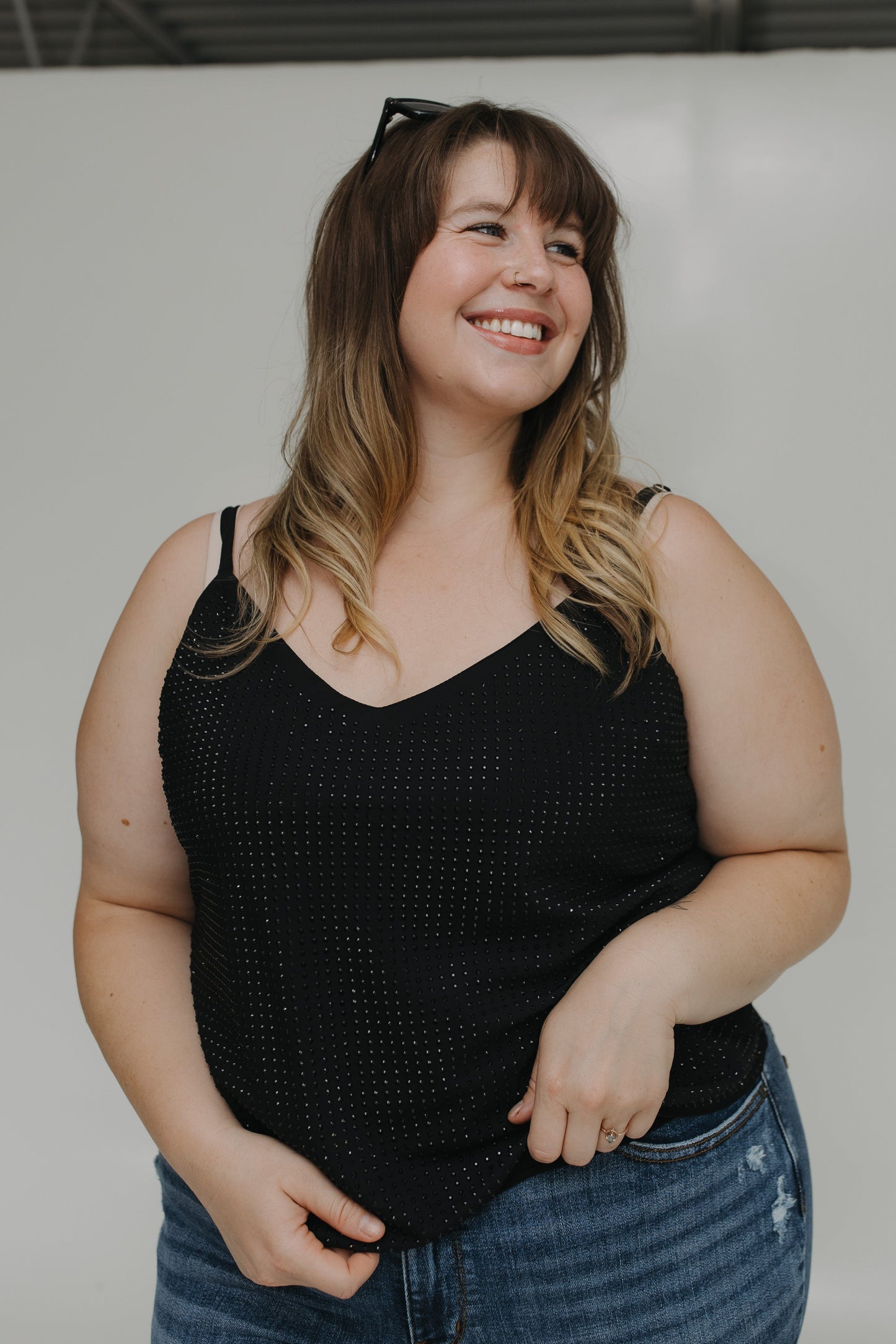 Woman wearing a black tank top and blue jeans with a neutral background