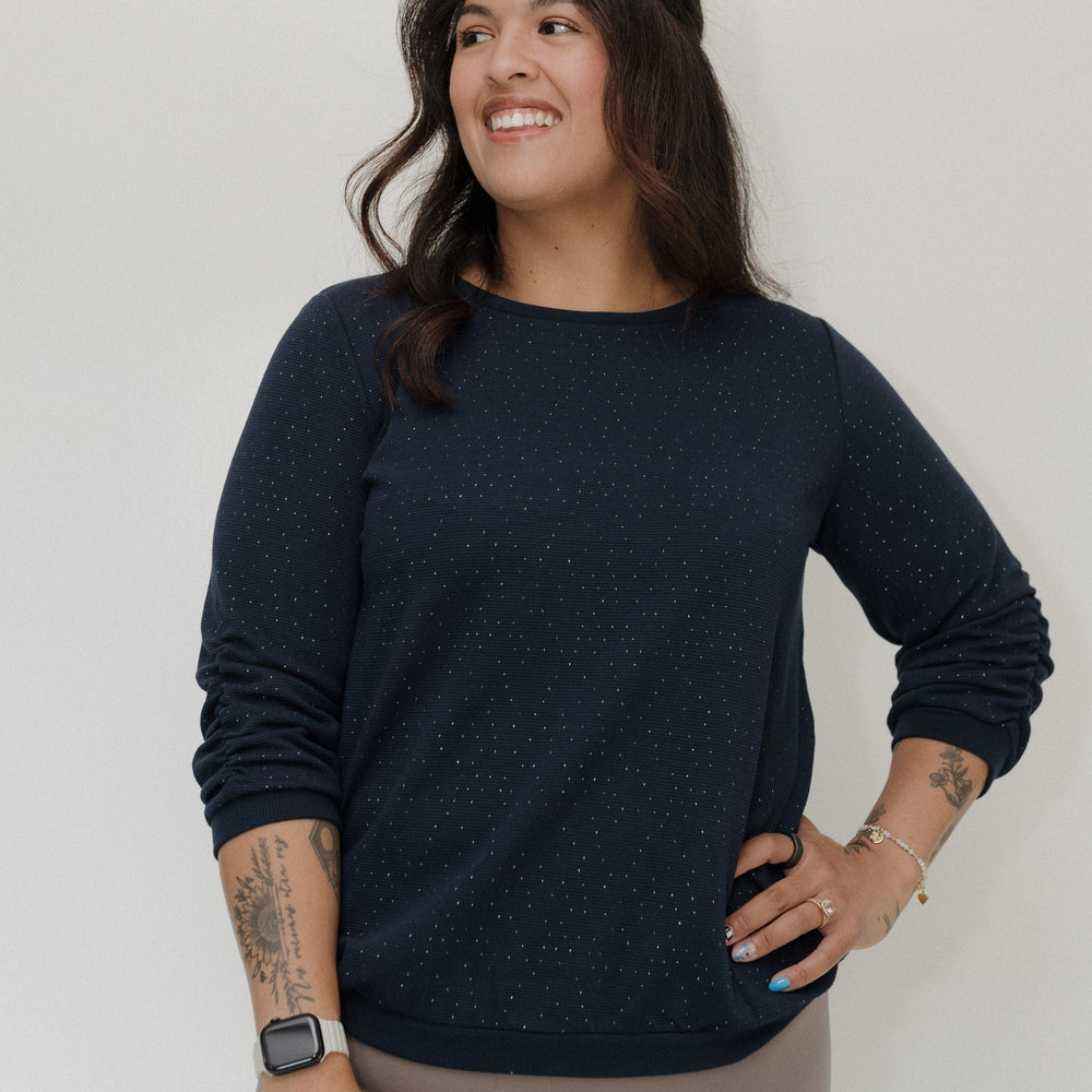 Woman wearing a navy blue sweater and beige pants against a white background