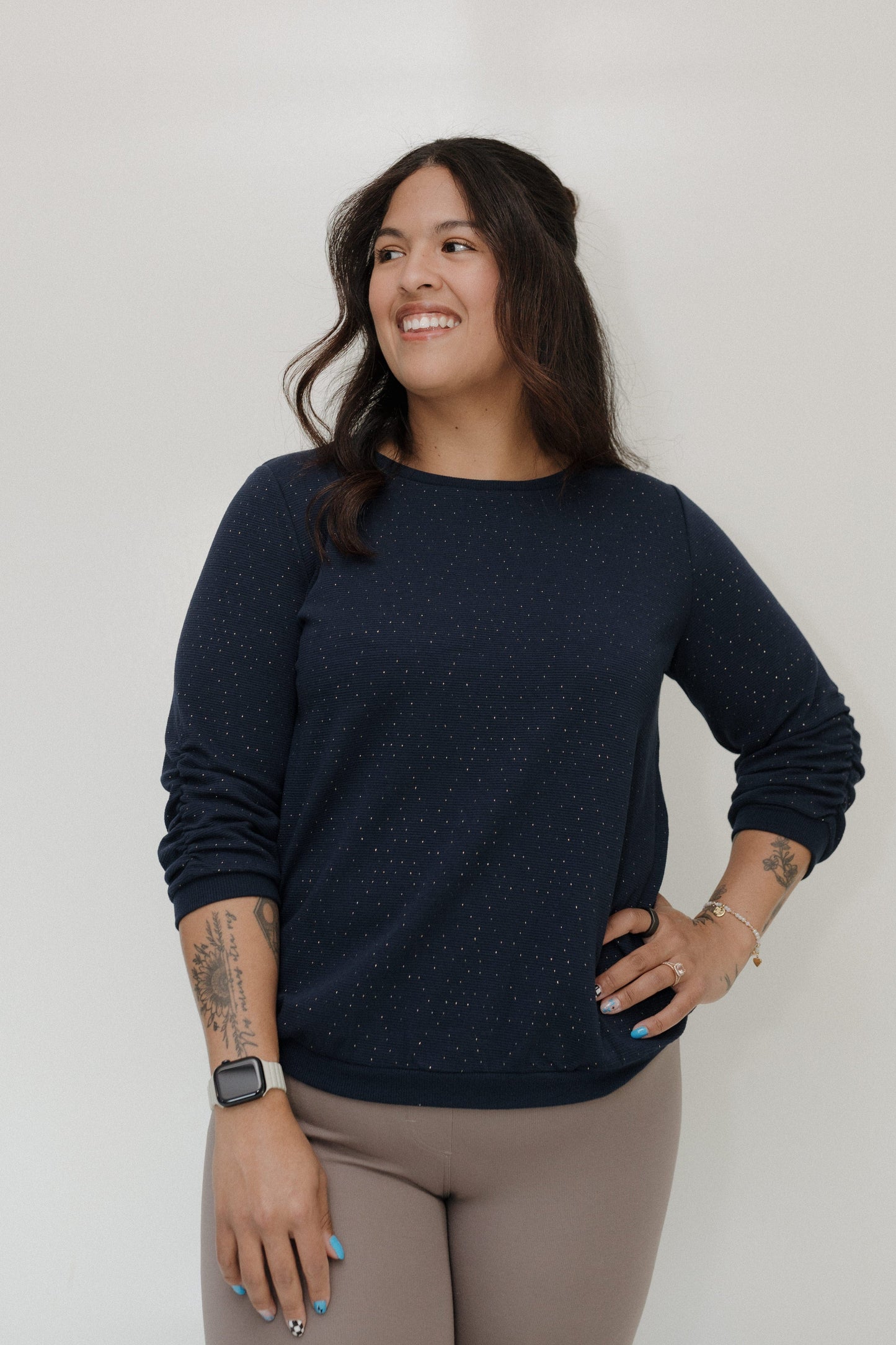 Woman wearing a navy blue sweater and beige pants against a white background