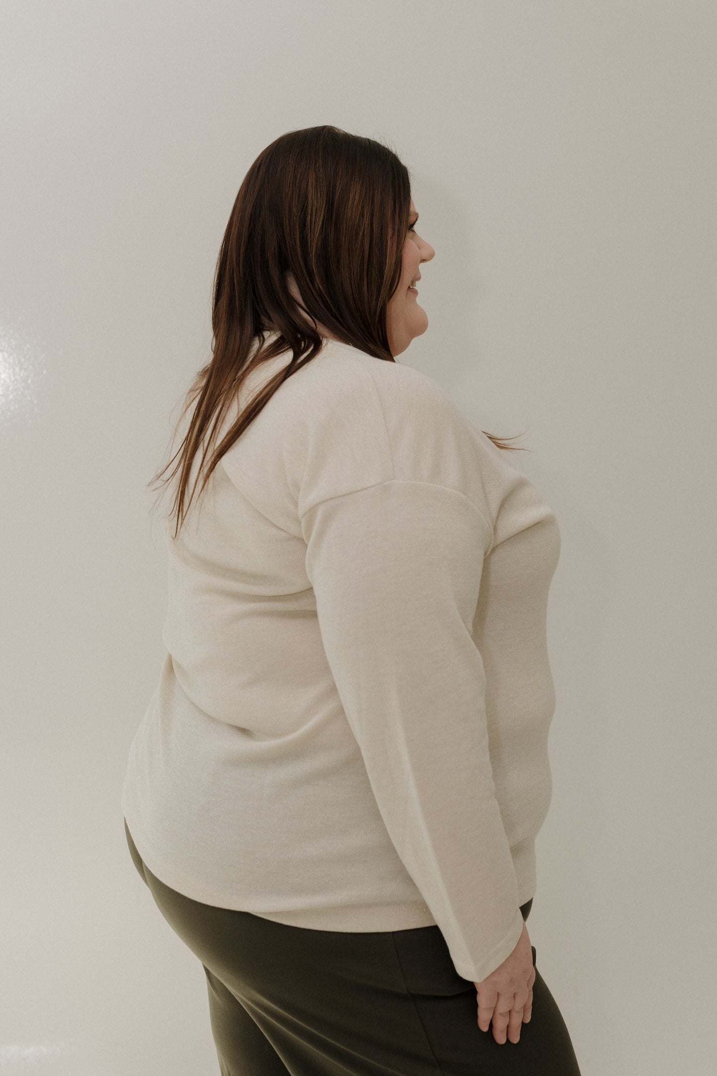 Person wearing a beige sweater and green pants against a plain background