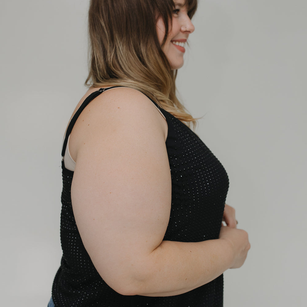 Woman wearing a black sleeveless top and blue jeans against a plain background