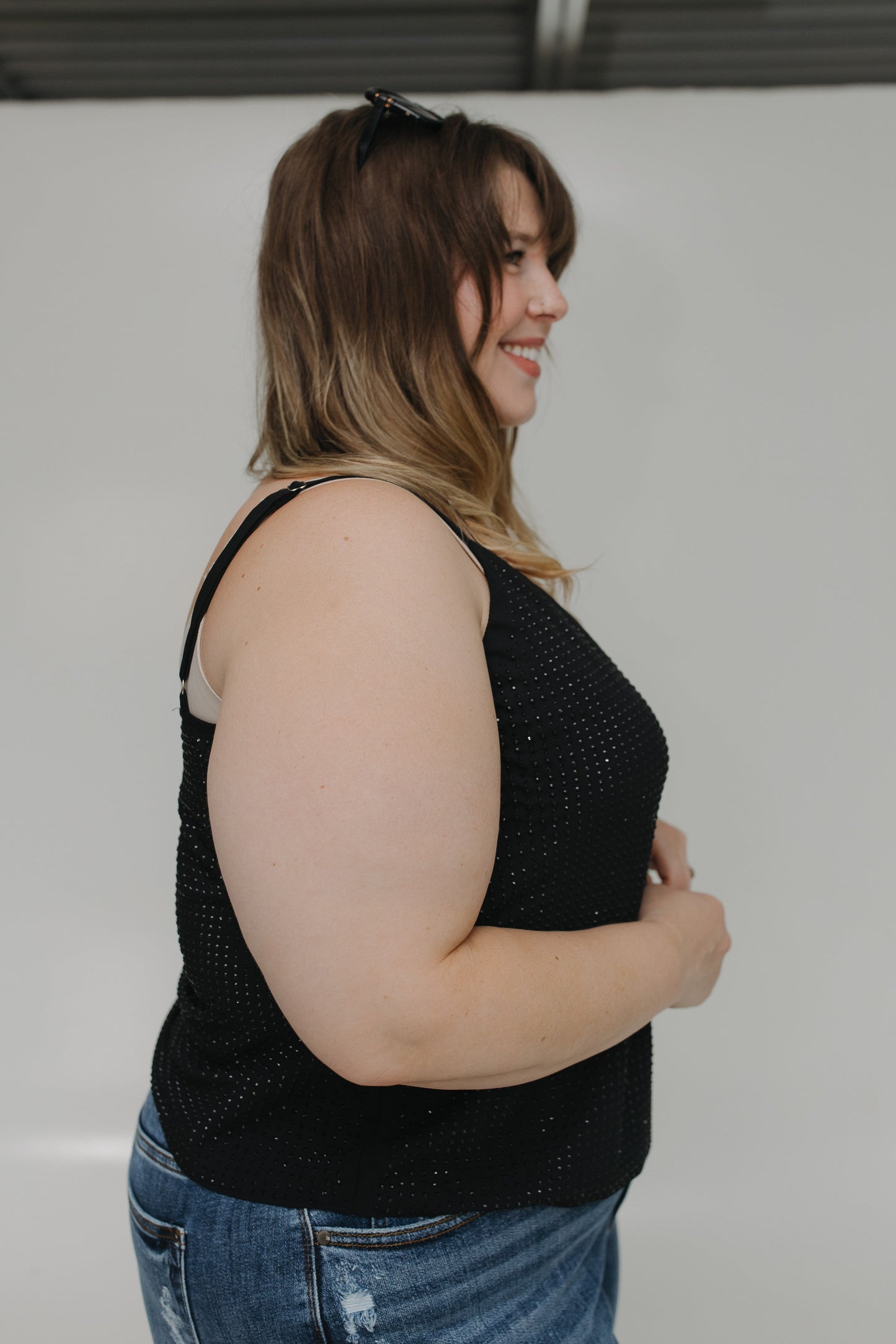 Woman wearing a black sleeveless top and blue jeans against a plain background