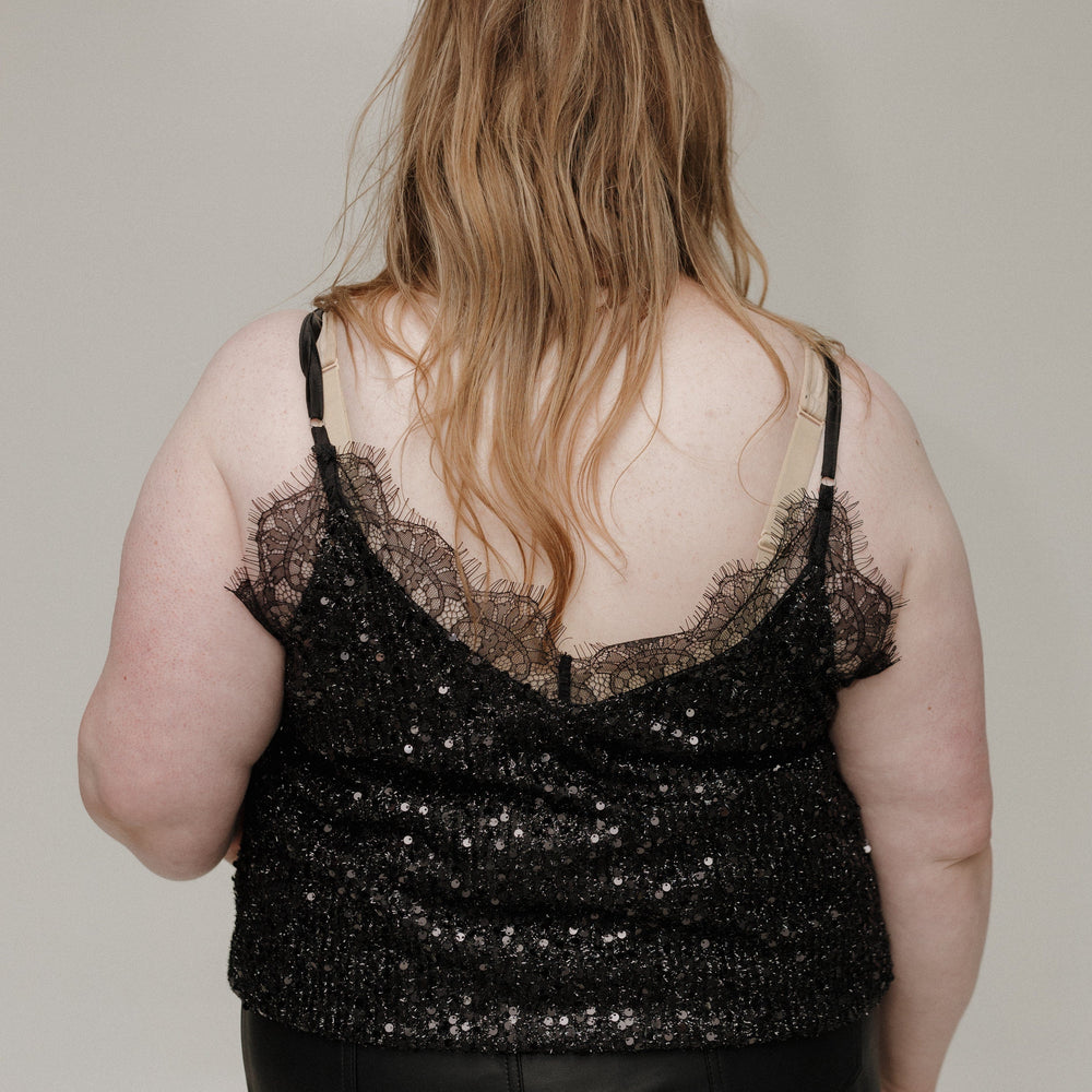 Person wearing a black sequin top and black pants against a plain background