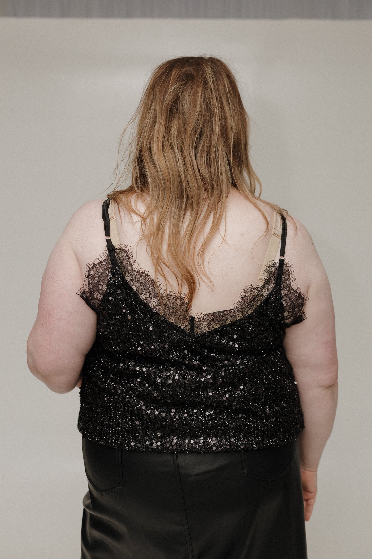 Person wearing a black sequin top and black pants against a plain background