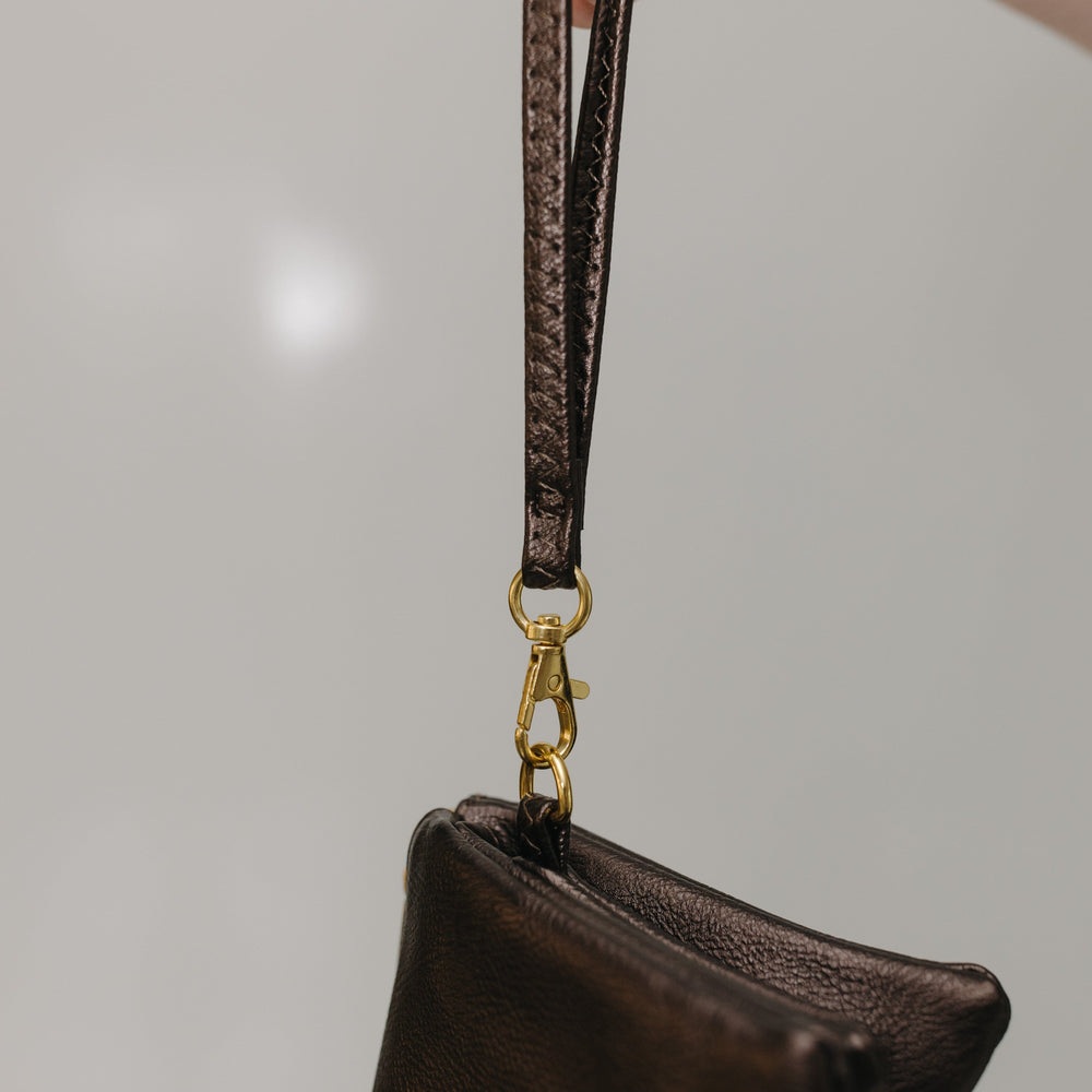 Brown leather pouch with a strap held by a hand against a neutral background
