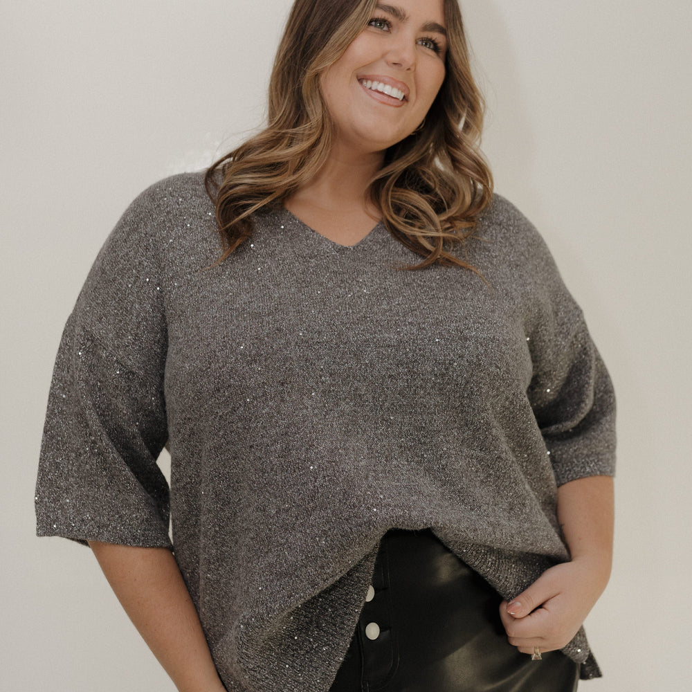 Woman wearing a gray sweater and black pants against a plain background