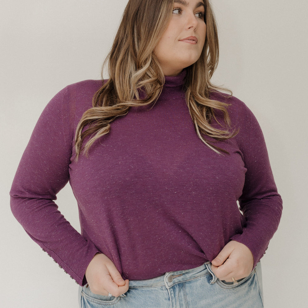 Woman wearing a purple long-sleeve top and light blue jeans against a plain background