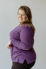 A person with long hair and glasses stands with their back to the camera, dressed in the SHIMMERY LIGHTWEIGHT TURTLENECK IN ROYALTY by Yesta paired with black pants, radiating timeless elegance against a neutral background.