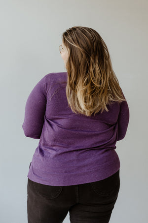 A person with long hair and glasses stands with their back to the camera, dressed in the SHIMMERY LIGHTWEIGHT TURTLENECK IN ROYALTY by Yesta paired with black pants, radiating timeless elegance against a neutral background.