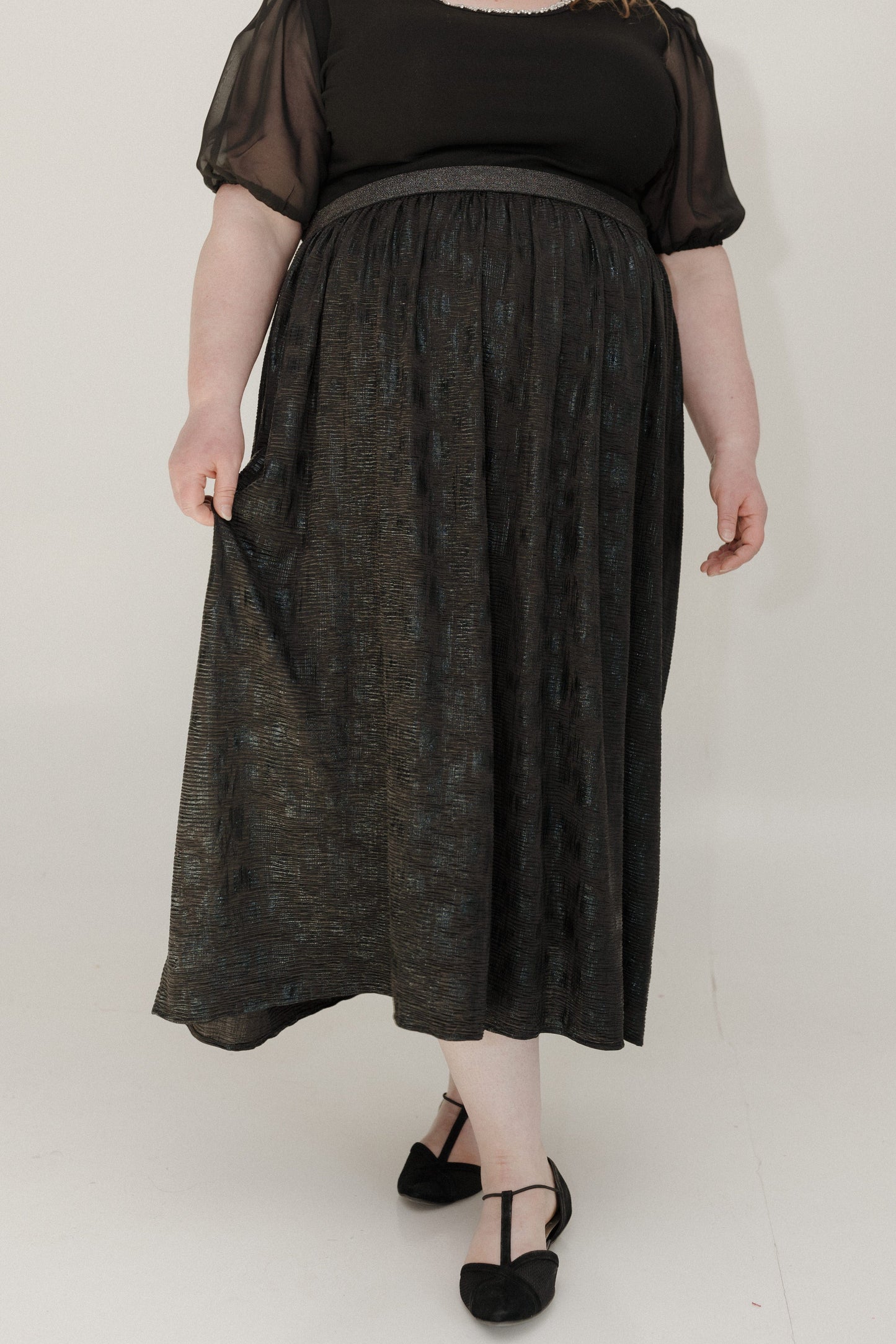 Person wearing a black top and dark gray skirt on a white background