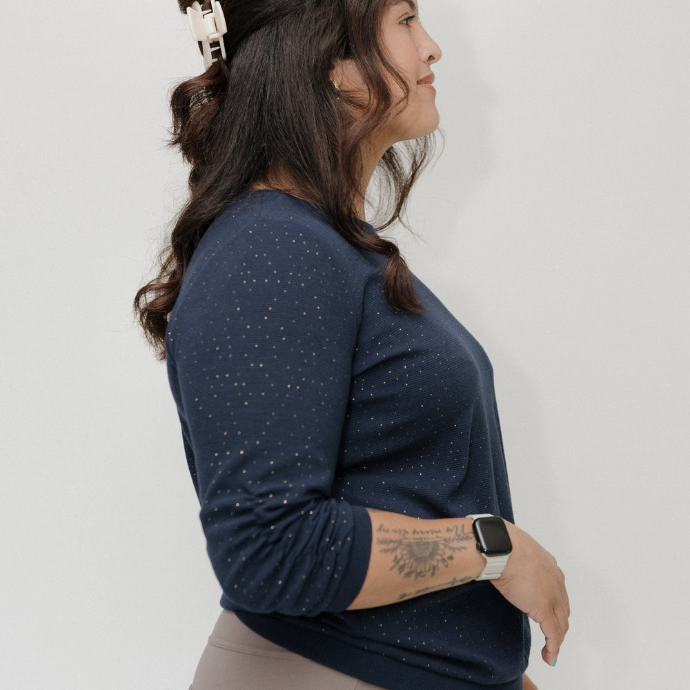 Woman wearing a navy blue long-sleeve top and beige pants against a white background