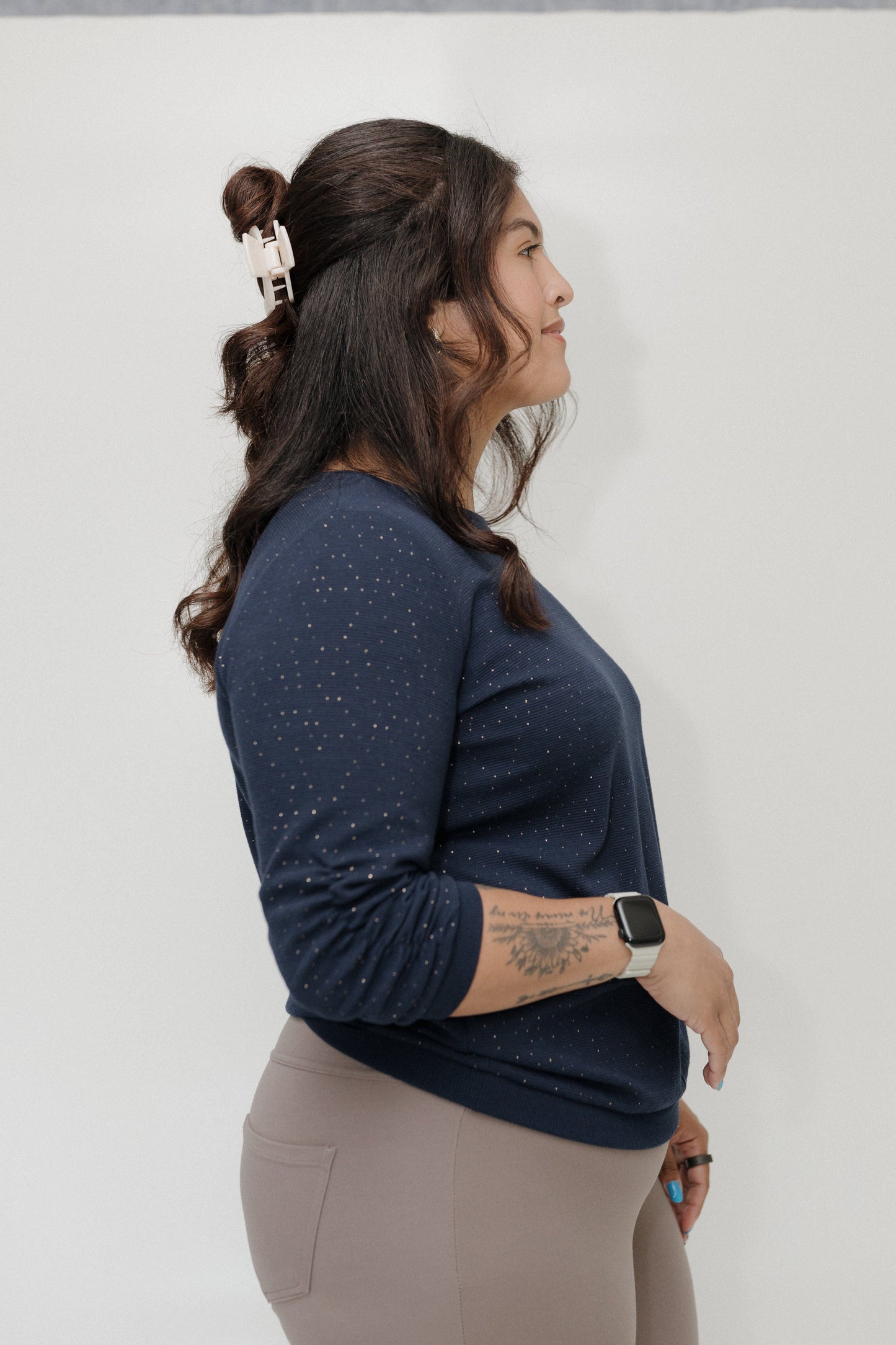 Woman wearing a navy blue long-sleeve top and beige pants against a white background
