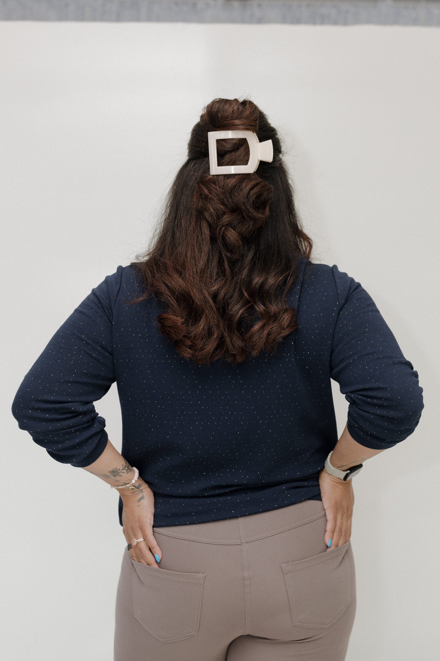 Person wearing a navy sweater and beige pants with a white belt buckle on a plain background