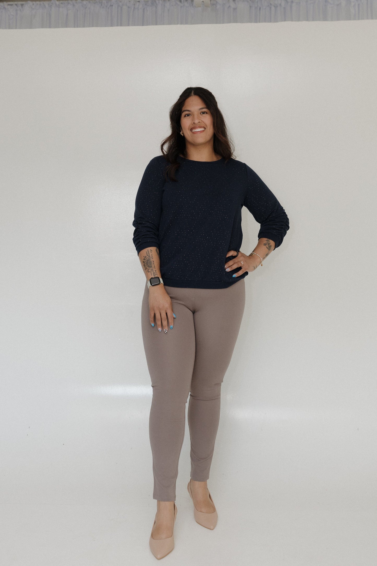 Woman wearing a navy sweater and beige leggings against a white background