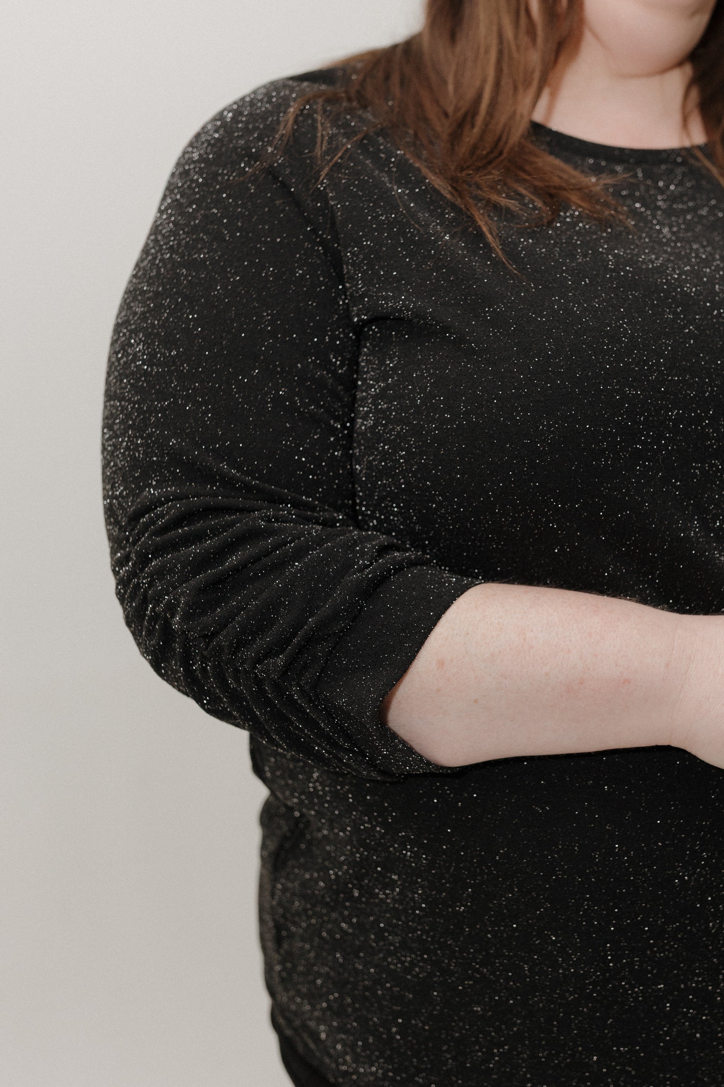 Person wearing a black glittery dress against a plain background