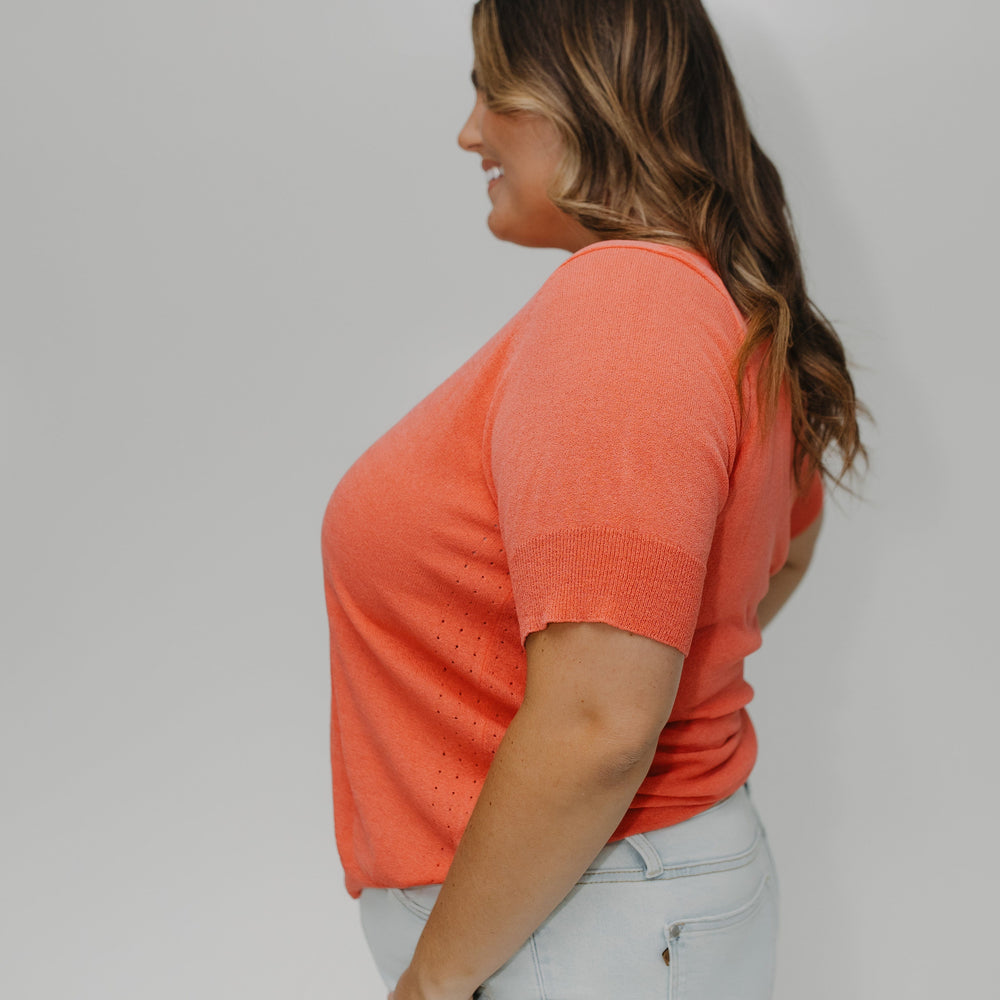 Woman wearing an orange shirt and light blue jeans against a white background