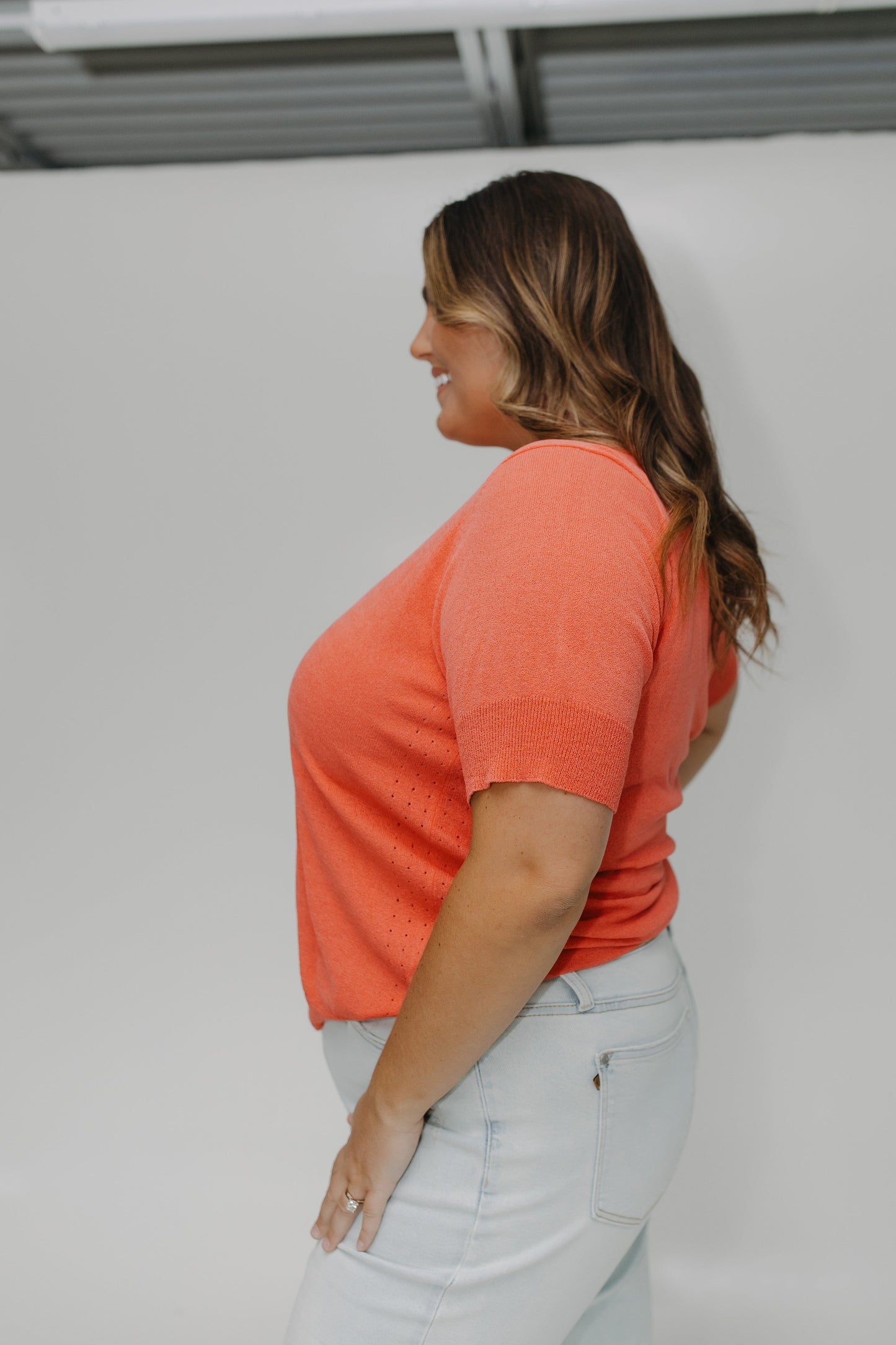 Woman wearing an orange shirt and light blue jeans against a white background
