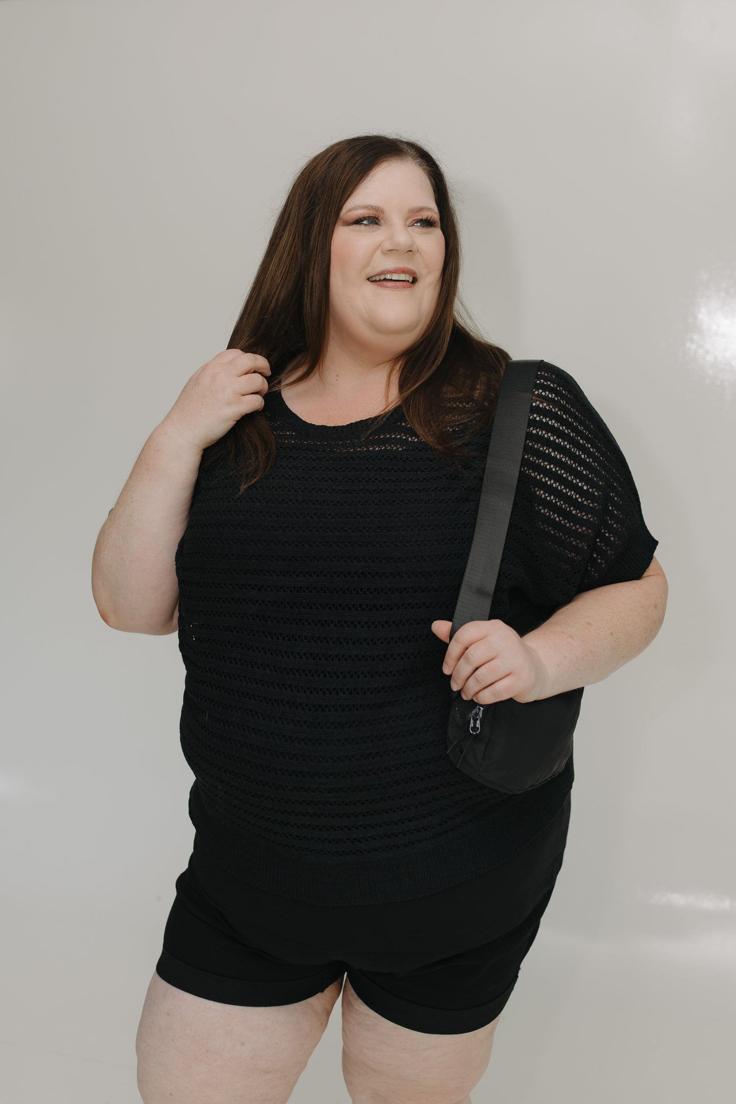 Woman wearing a black outfit with a shoulder bag against a plain background