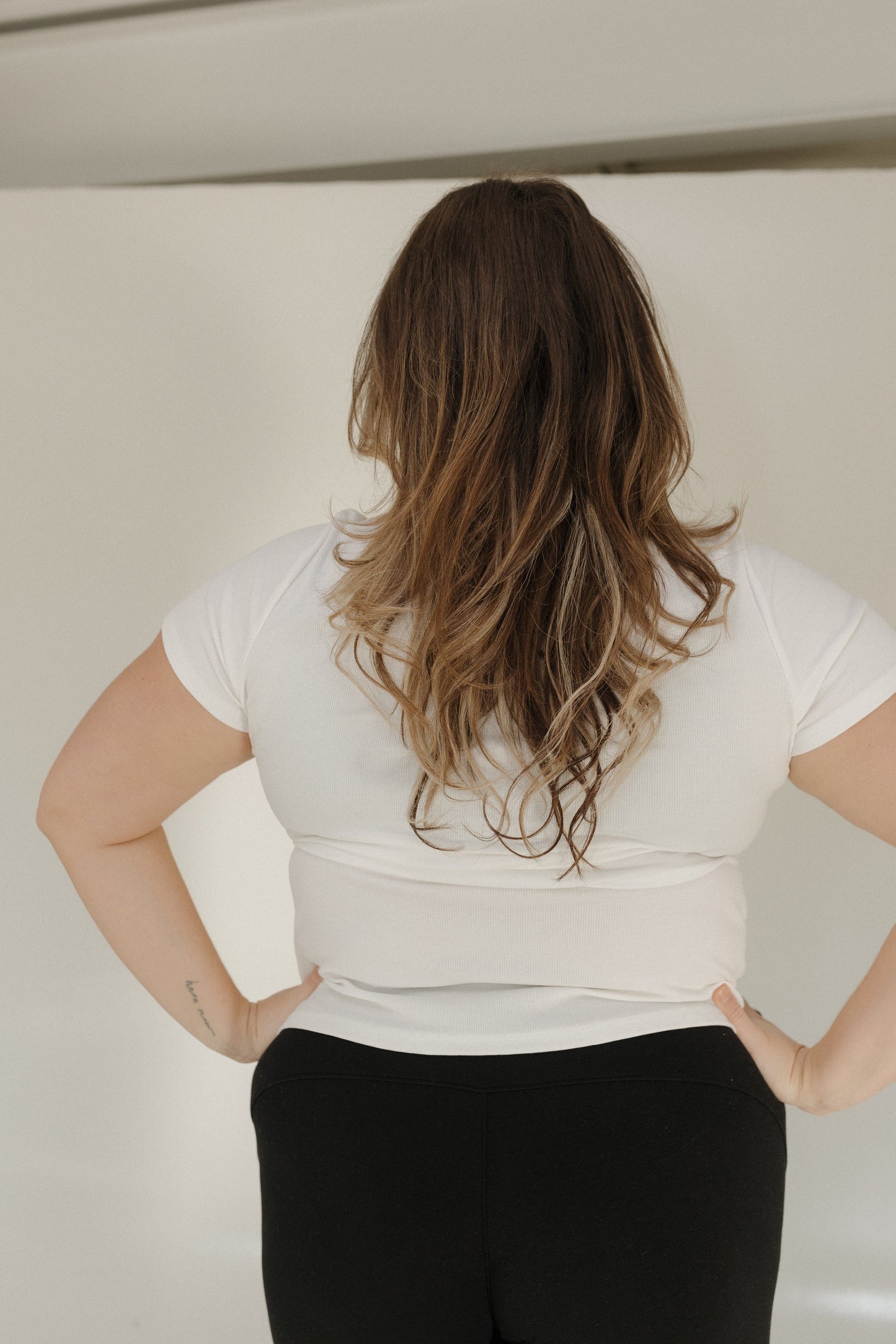 Person wearing a white top and black pants with hands on hips against a plain background