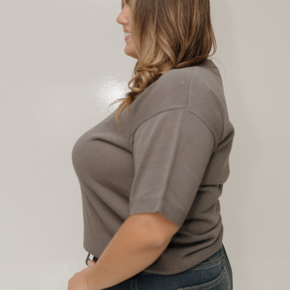 Woman wearing a brown shirt and blue jeans against a plain background