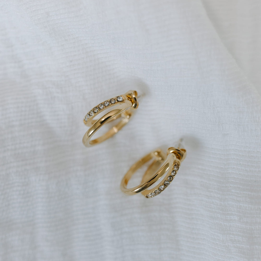 Gold hoop earrings with small diamonds on a white fabric background