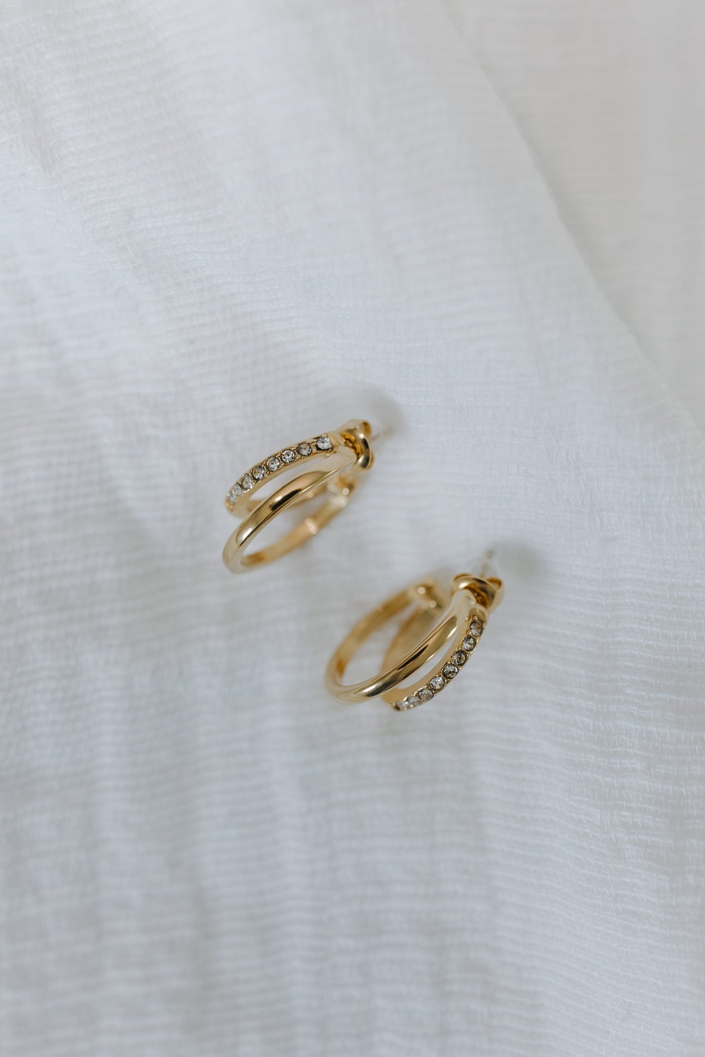 Gold hoop earrings with small diamonds on a white fabric background