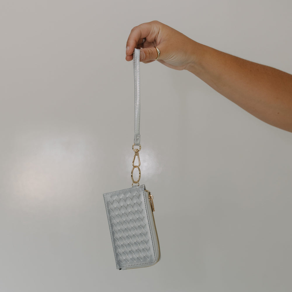 Hand holding a small textured wallet with a strap against a plain background