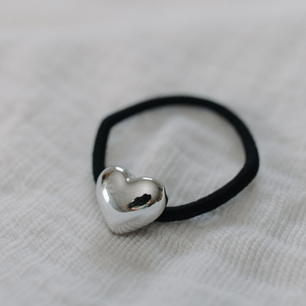 Black hair tie with a silver heart-shaped charm on a light fabric background