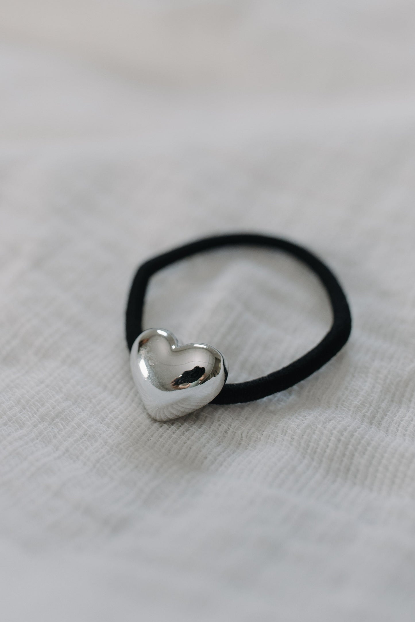 Black hair tie with a silver heart-shaped charm on a light fabric background