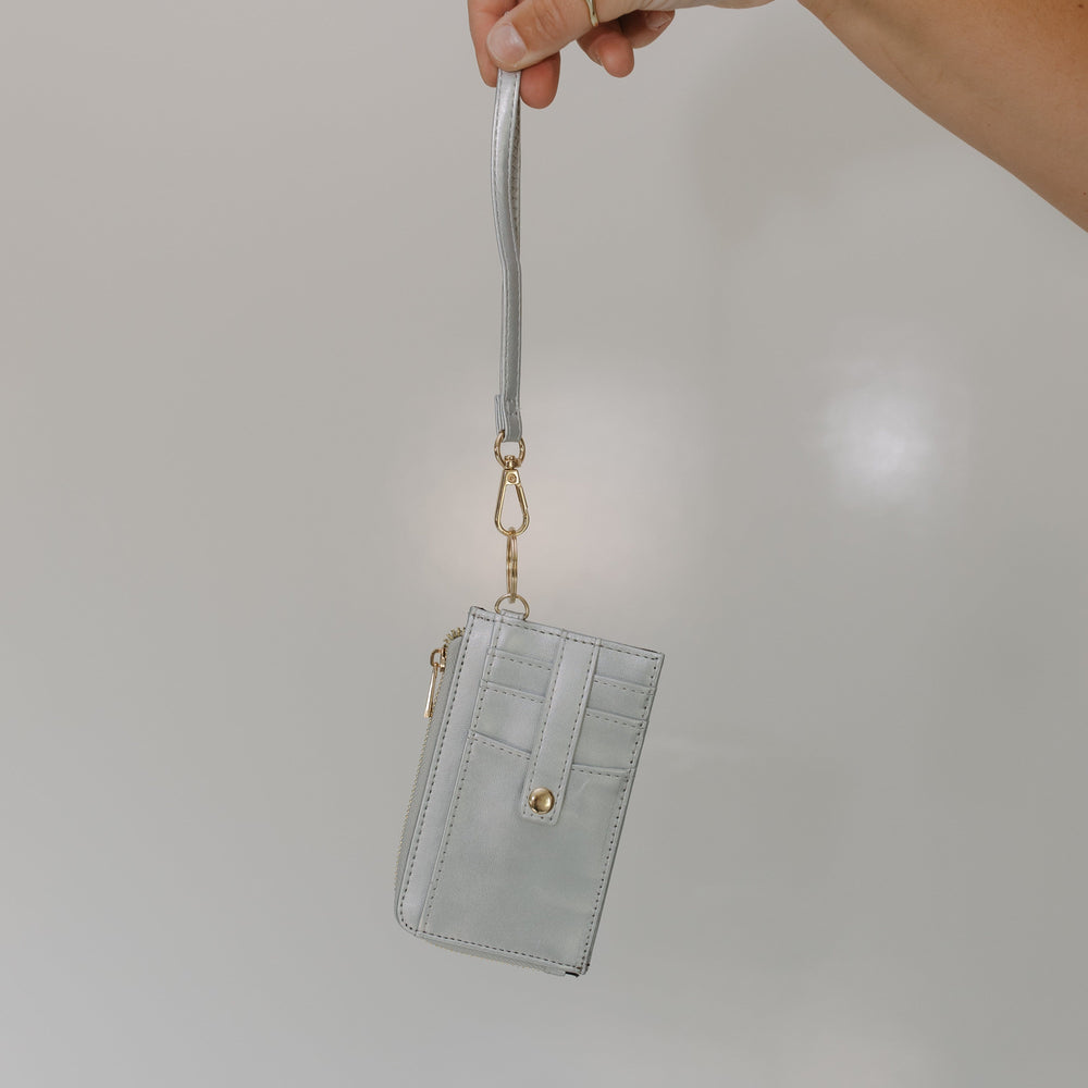 Hand holding a light gray wallet with a strap against a plain background