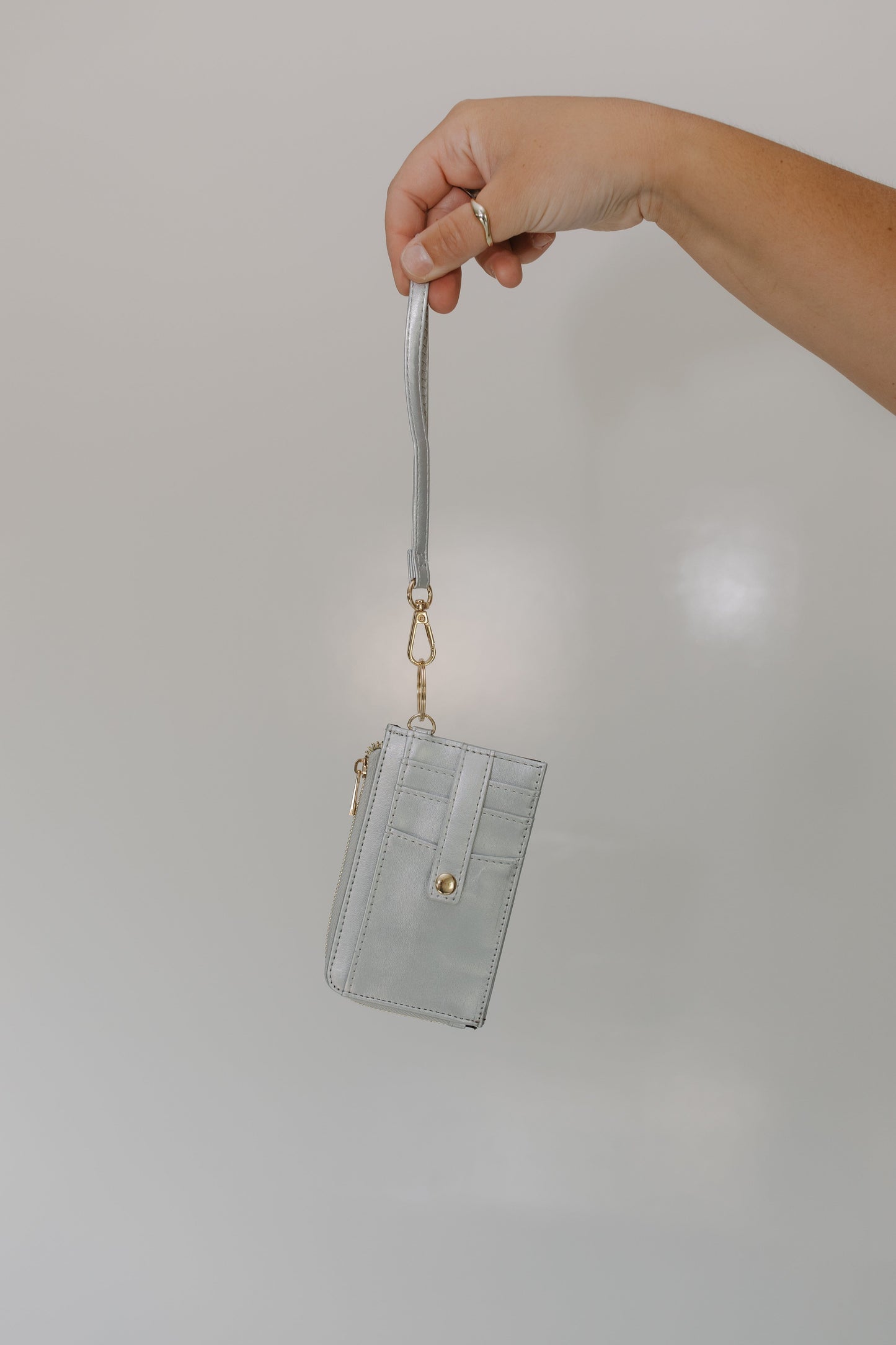 Hand holding a light gray wallet with a strap against a plain background