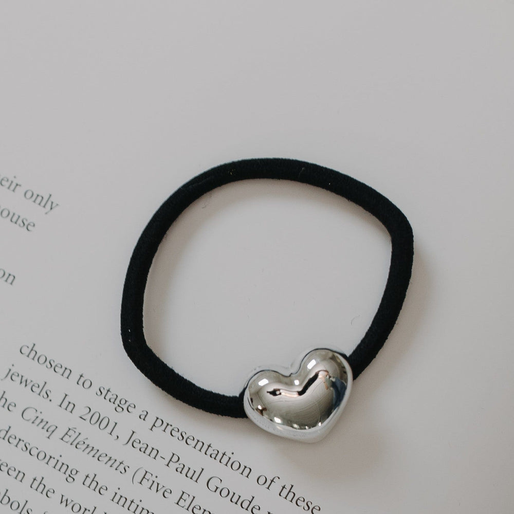 Black hair elastic with a silver heart-shaped charm on a book page