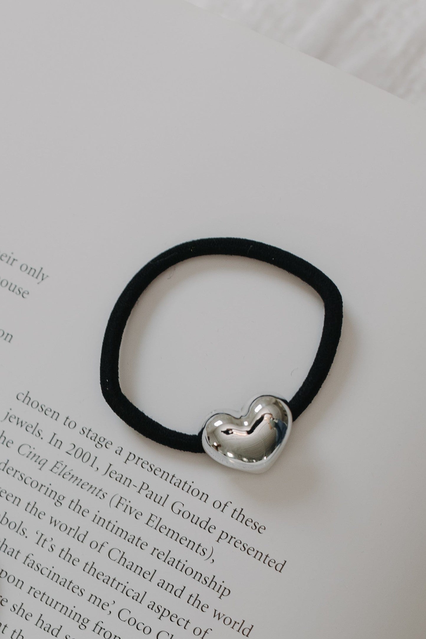 Black hair elastic with a silver heart-shaped charm on a book page