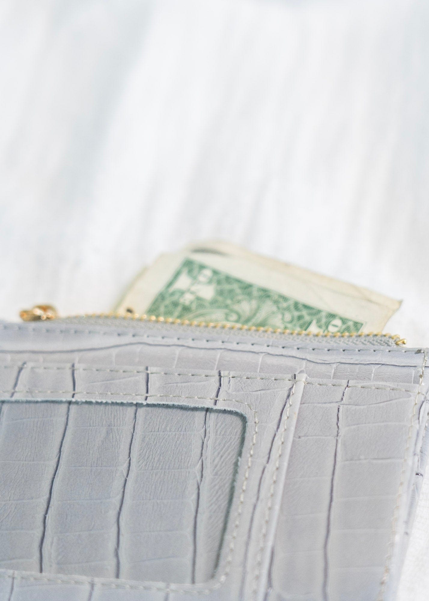 A smoky croc wallet crafted from faux leather rests on intertwined wooden branches, with a green potted plant in the background. This sleek cardholder is RFID protected, offering both style and security in one elegant package.