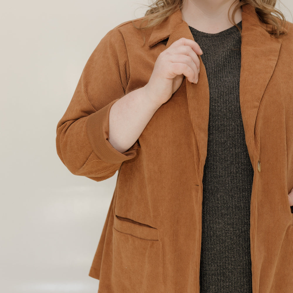 Person wearing a brown jacket over a dark dress against a plain background