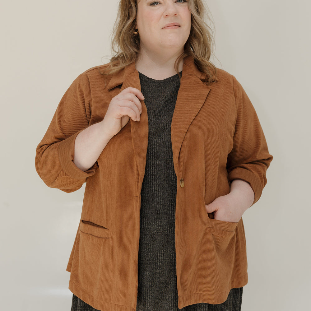 Woman wearing a brown jacket over a dark dress against a plain background