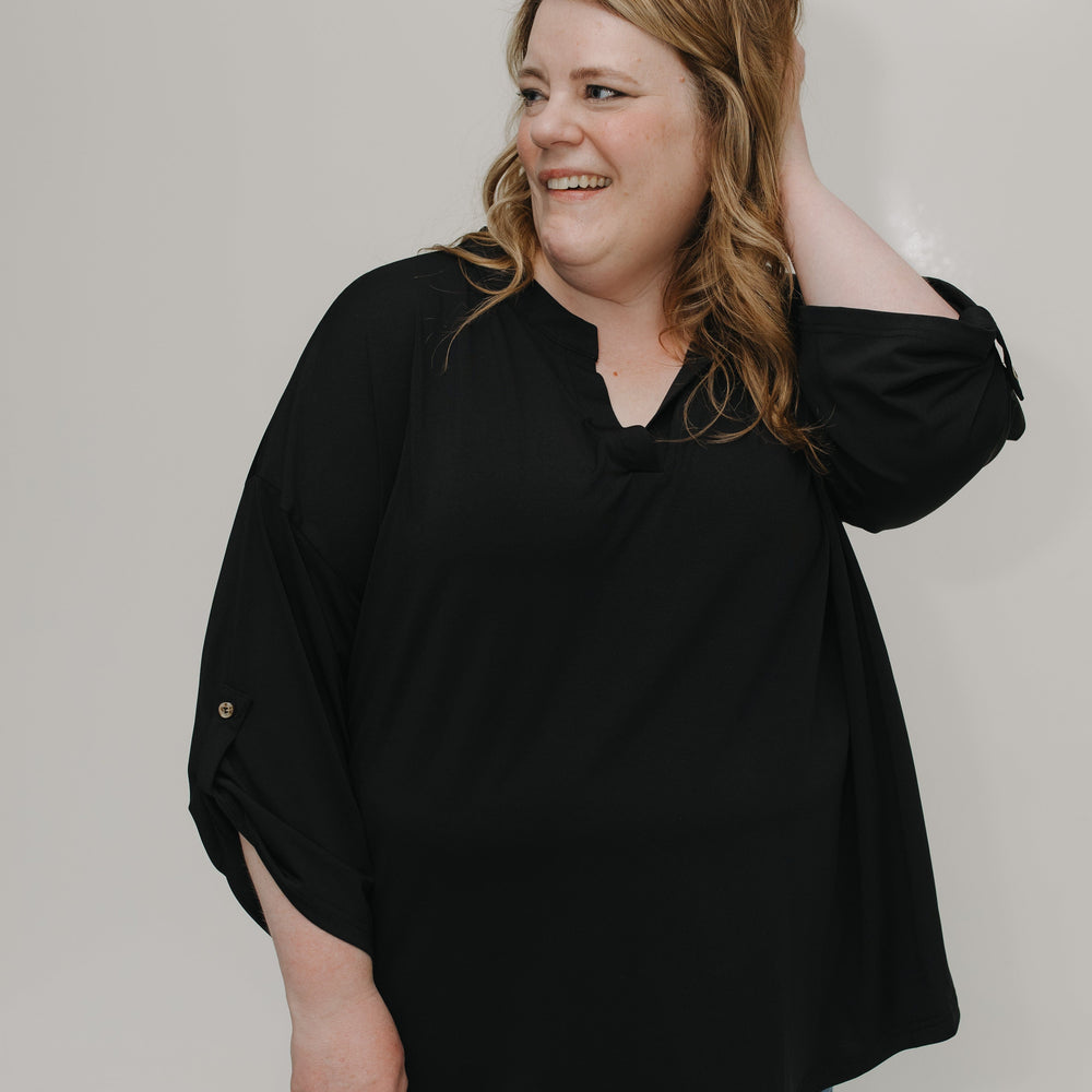 Woman wearing a black top and blue jeans against a plain background