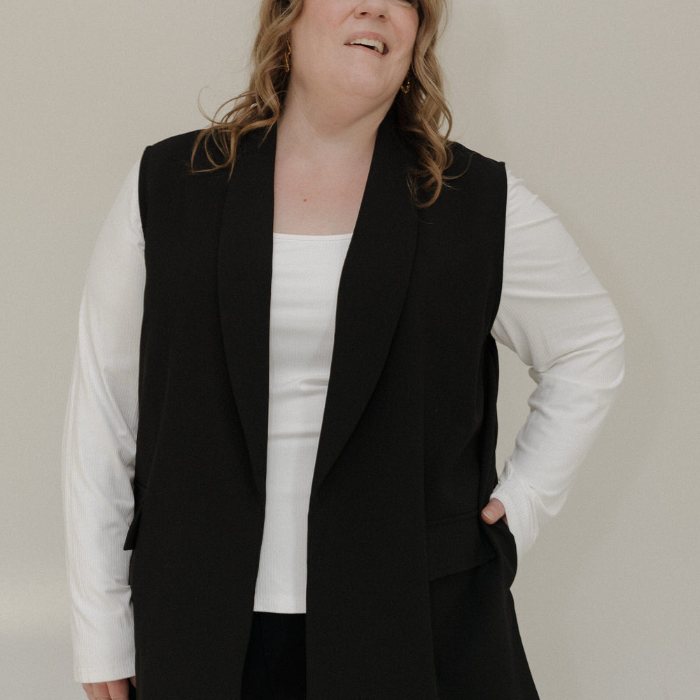 Person wearing a black vest over a white shirt on a plain background