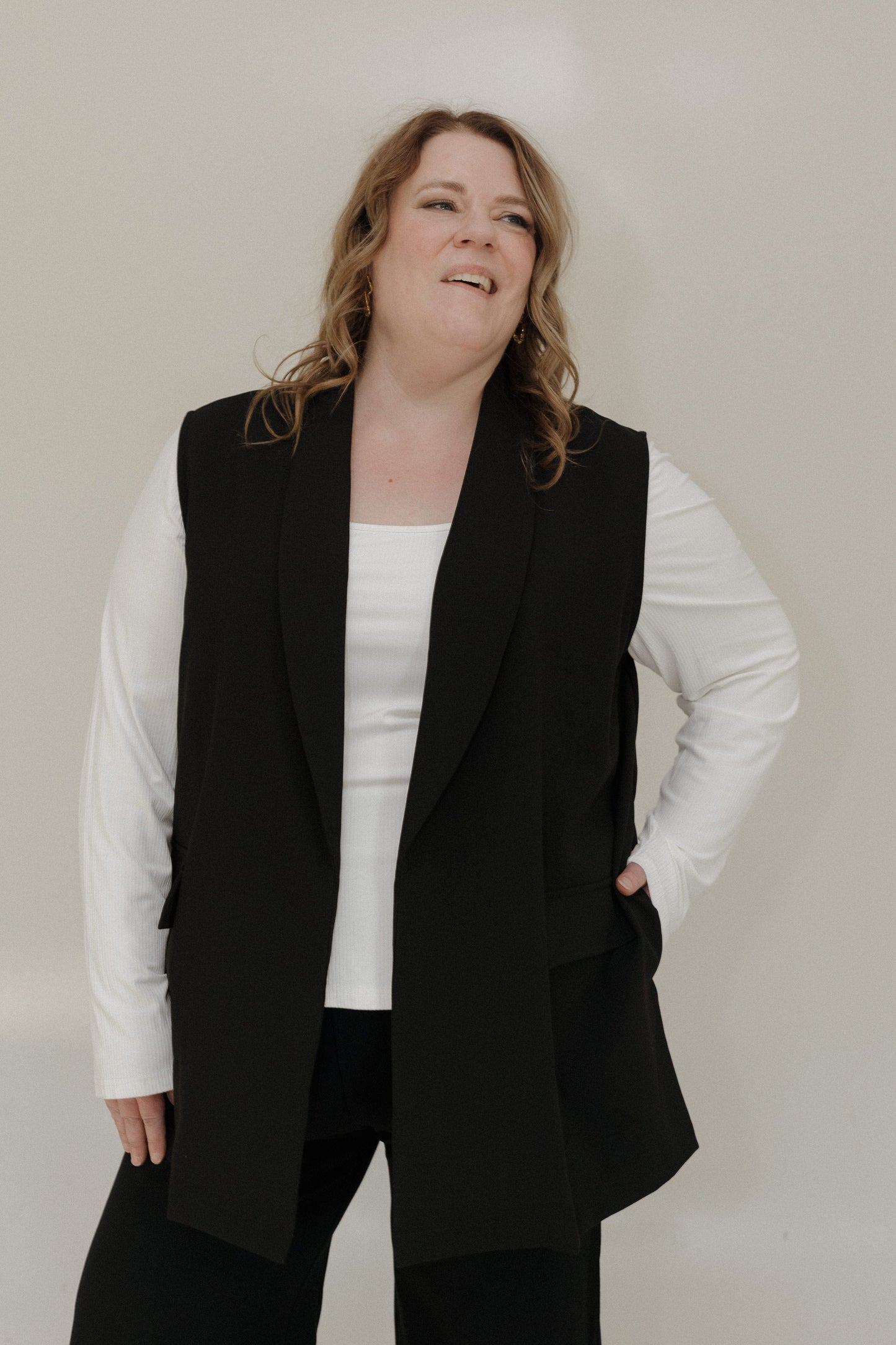 Person wearing a black vest over a white shirt on a plain background