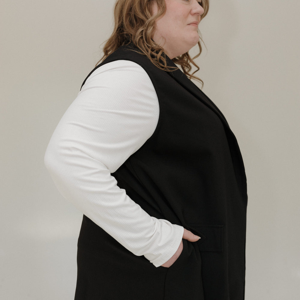 Person wearing a black vest over a white long-sleeve shirt against a plain background