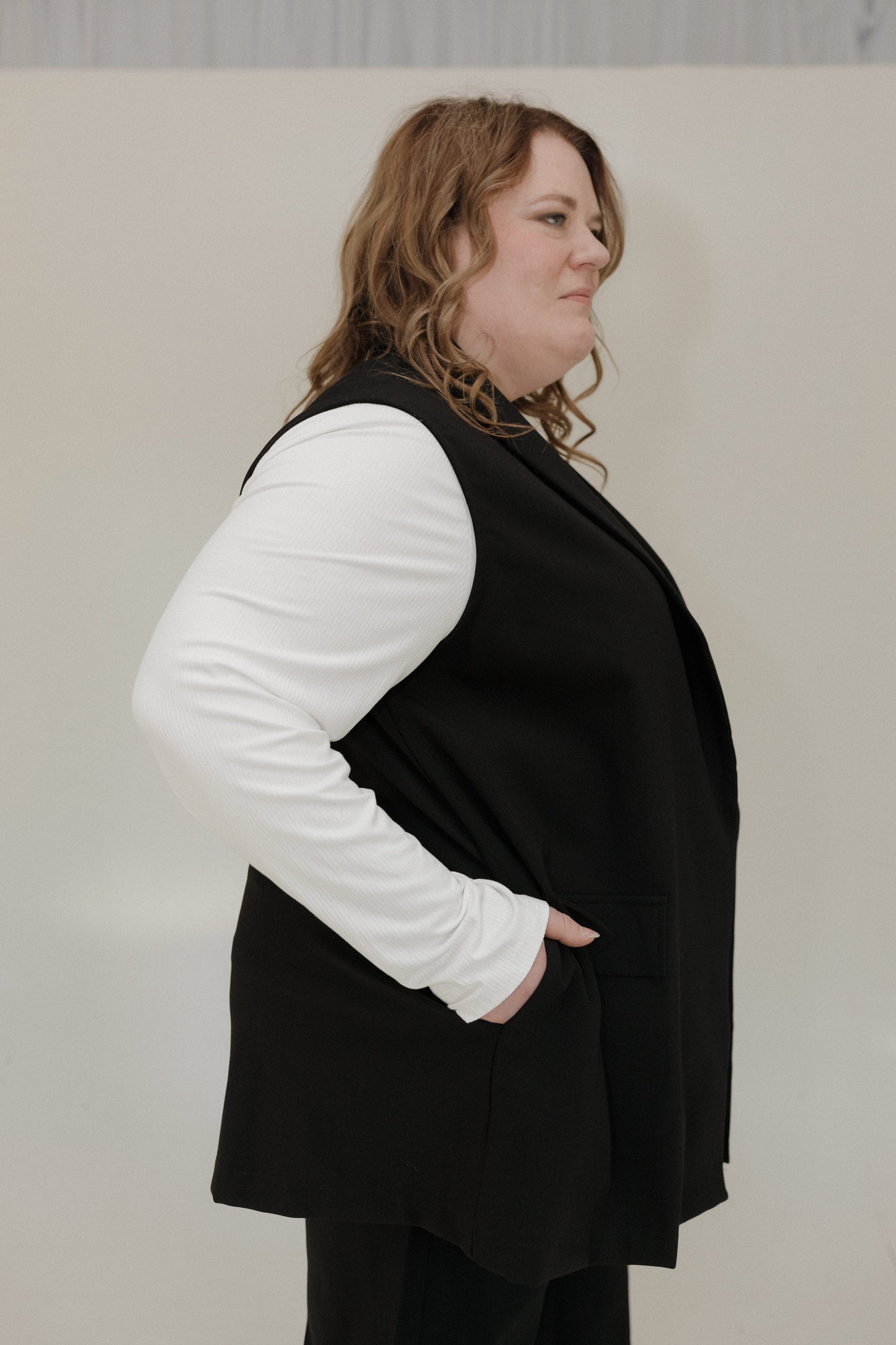 Person wearing a black vest over a white long-sleeve shirt against a plain background