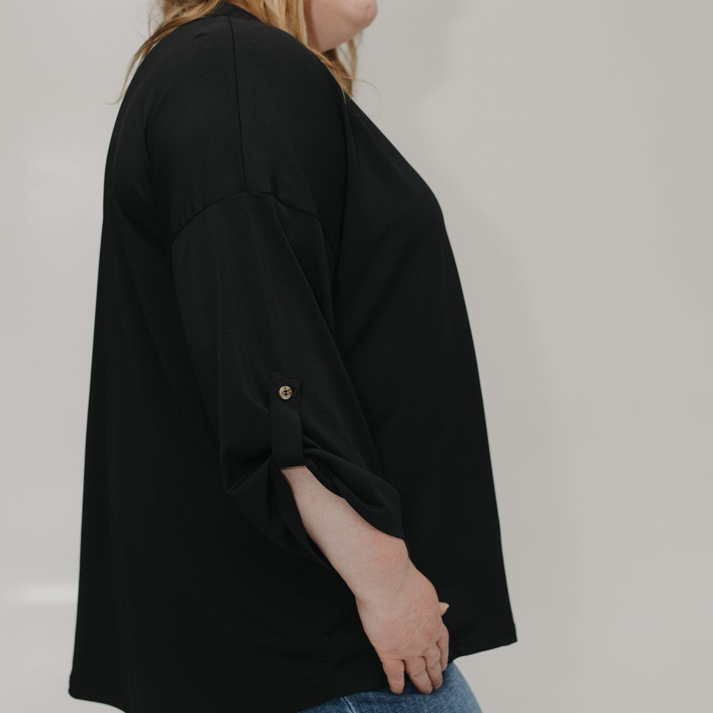Person wearing a black oversized shirt and blue jeans on a plain background