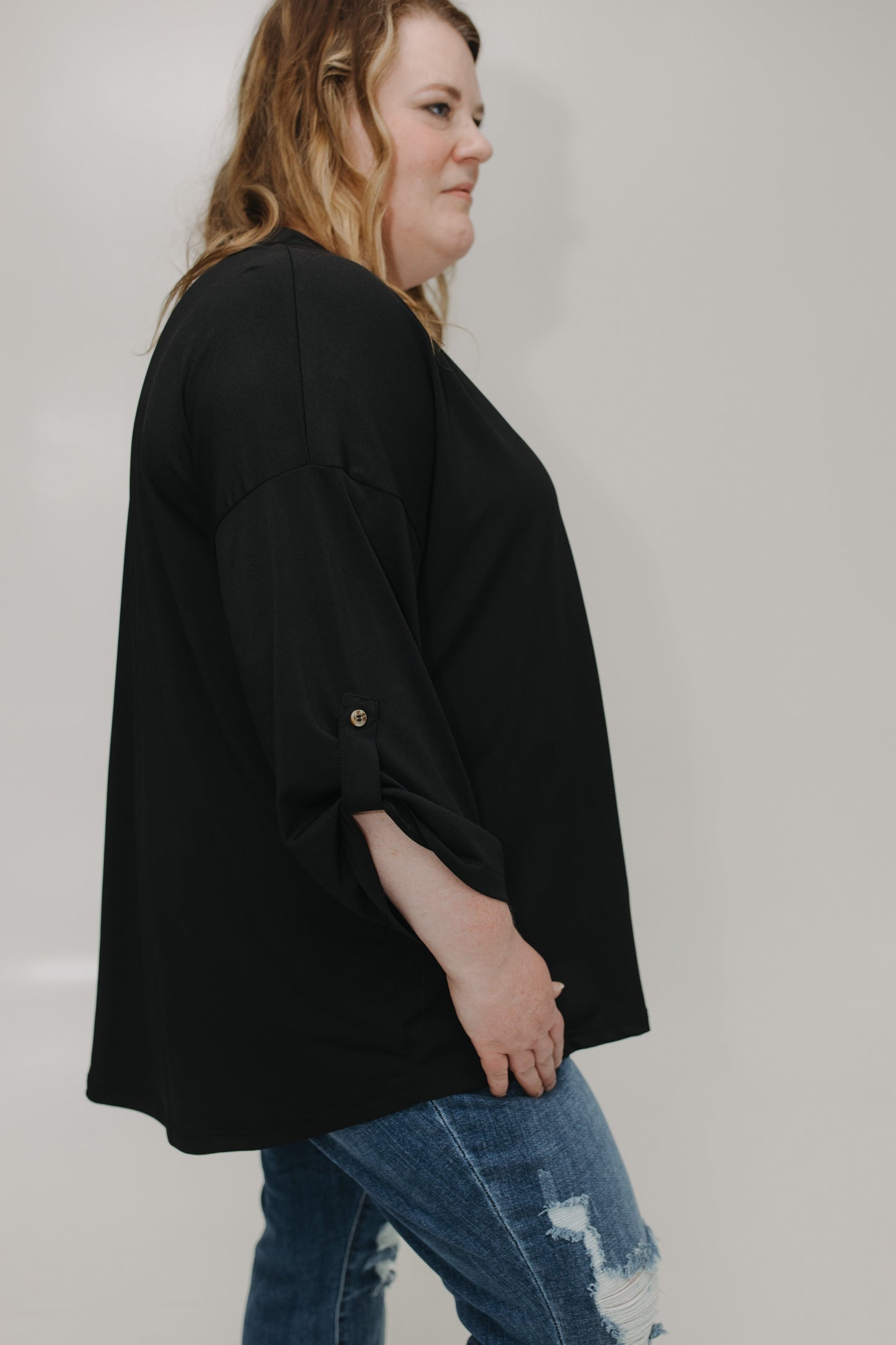 Person wearing a black oversized shirt and blue jeans on a plain background