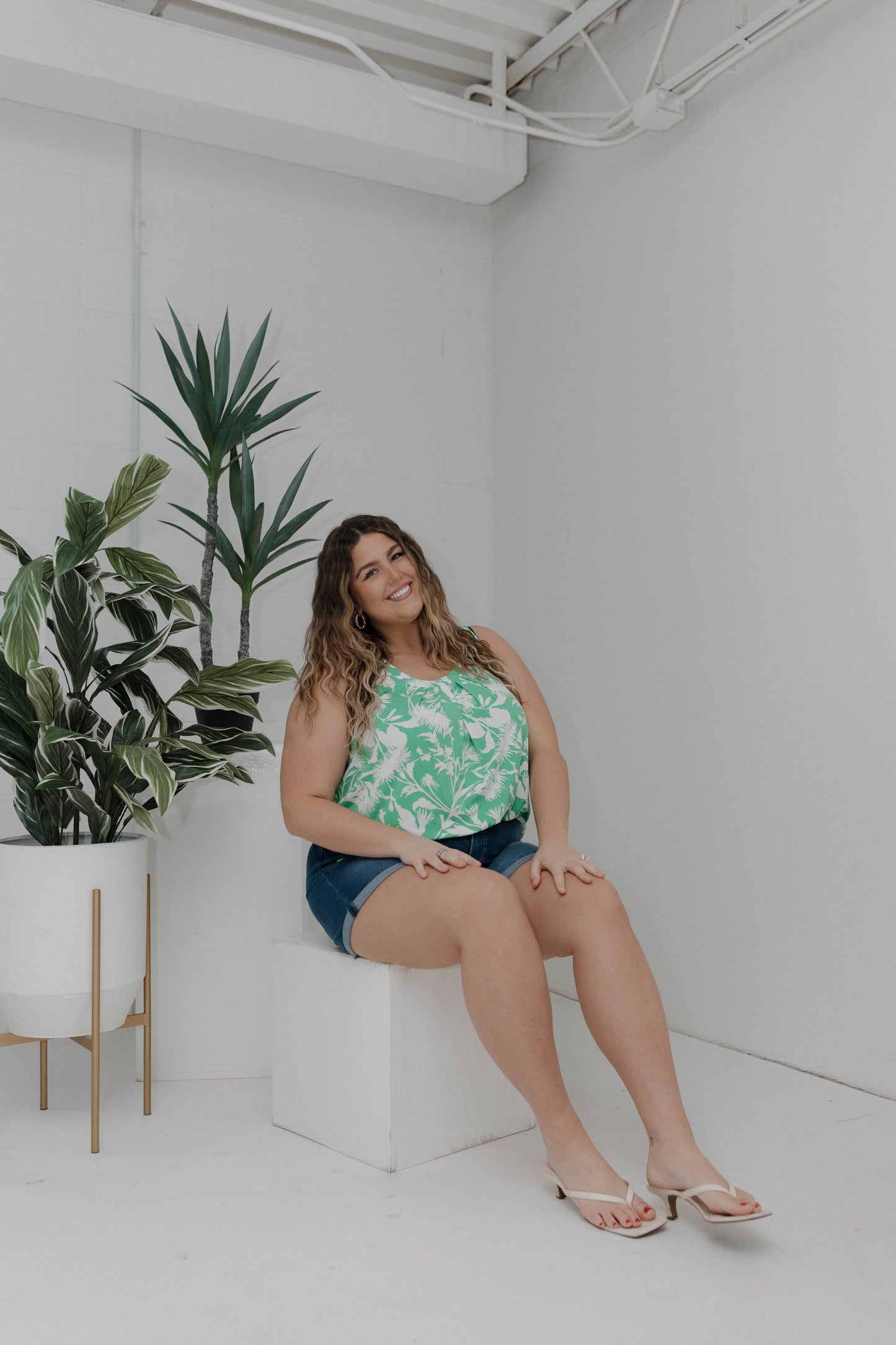 Woman sitting on a white block in a minimalistic room with plants