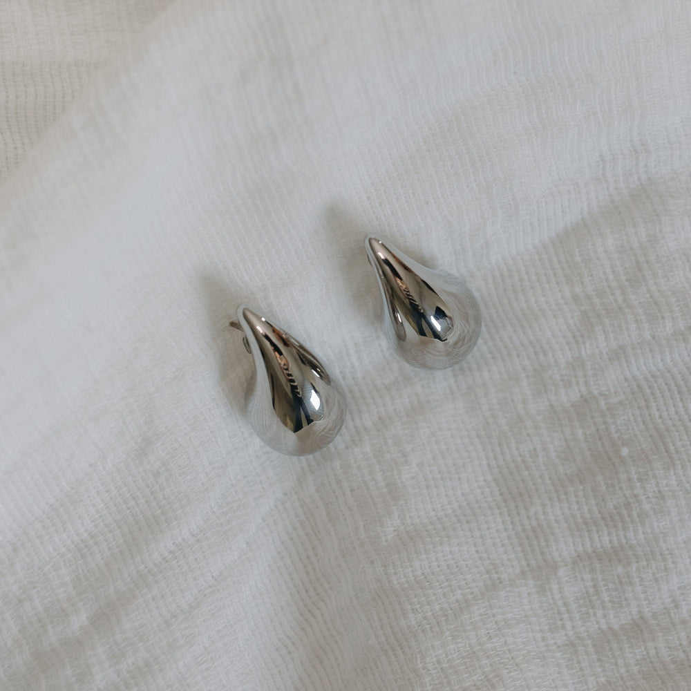 Pair of silver teardrop-shaped earrings on a light fabric background