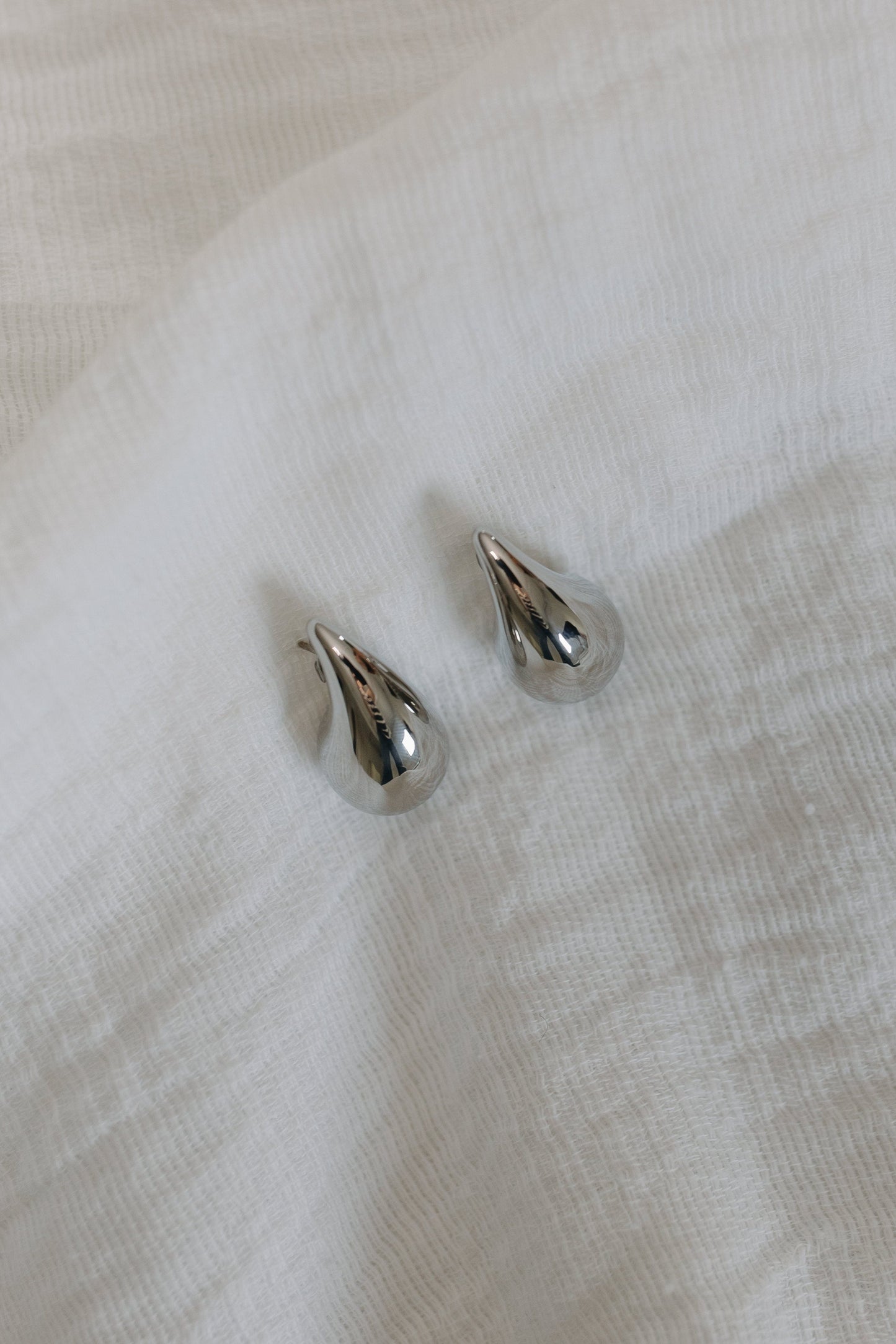 Pair of silver teardrop-shaped earrings on a light fabric background