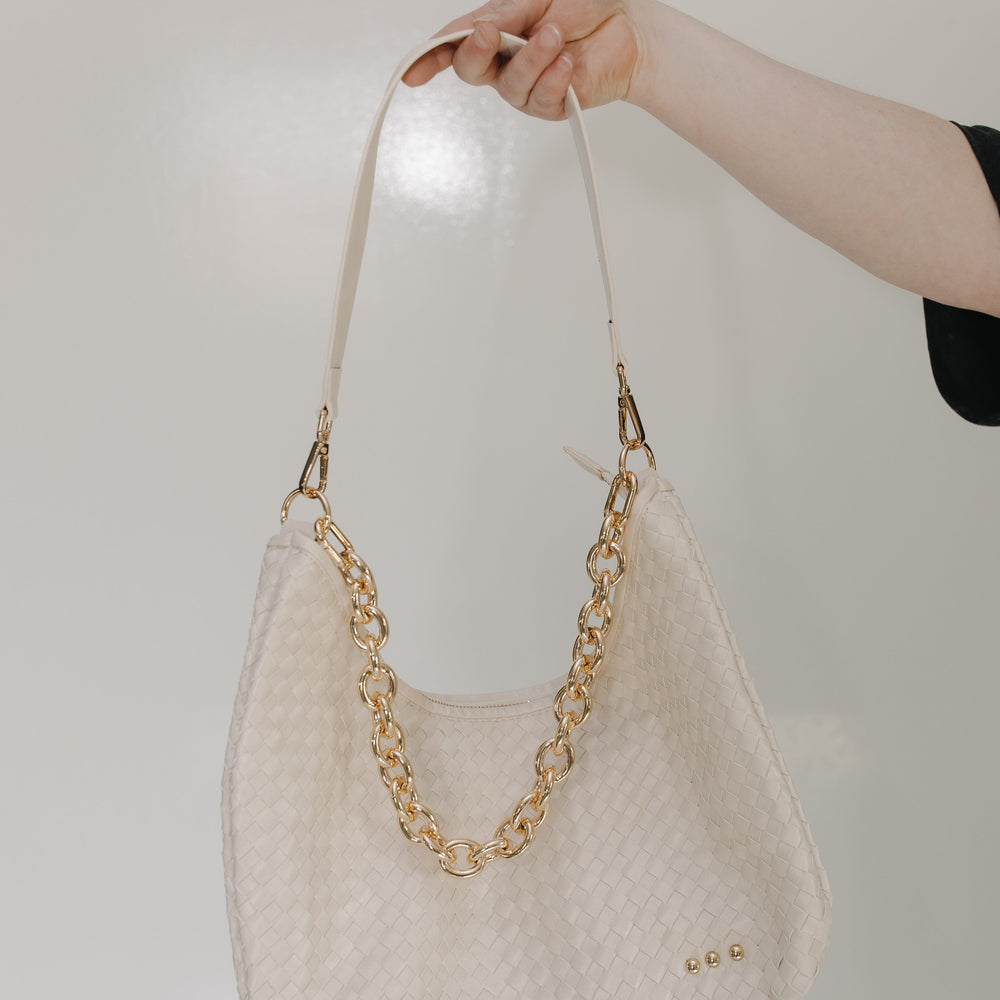 Cream handbag with gold chain handle held by a hand against a light background