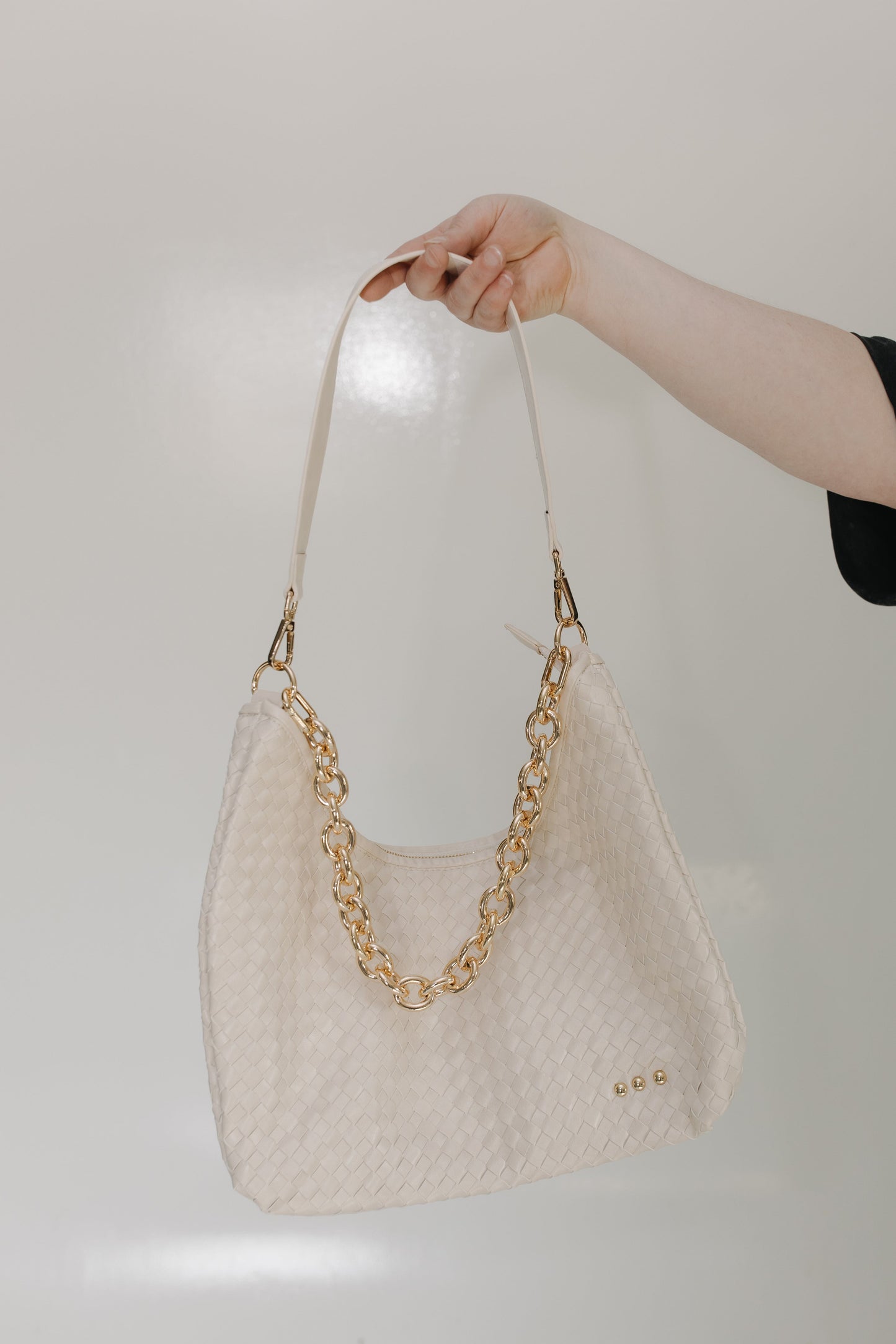 Cream handbag with gold chain handle held by a hand against a light background