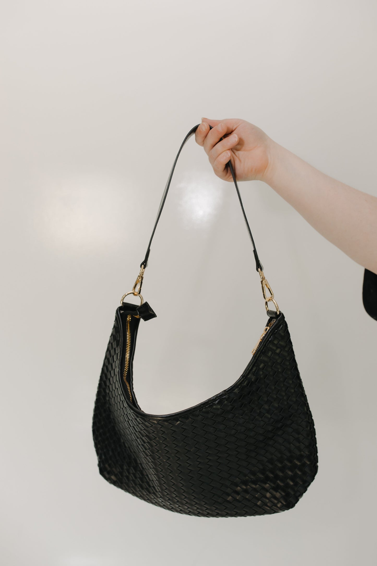 Black woven handbag held by a hand against a plain background